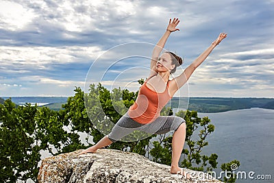 An attractive young woman doing a yoga pose for balance on the rock. Stock Photo