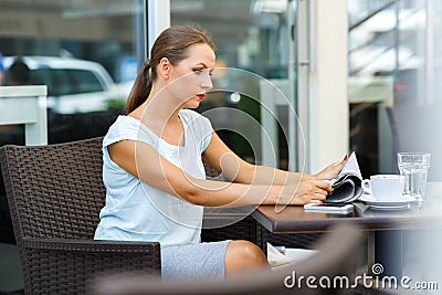 Attractive young woman reads a newspaper sitting in a cafe Stock Photo