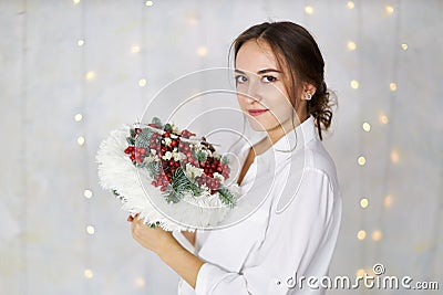 Attractive young woman stands with an original bouquet in her hands on a background of a light wall Stock Photo