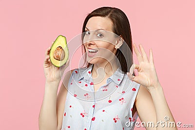 Attractive young woman in summer clothes showing OK gesture, hold fresh ripe green avocado fruit isolated on pink pastel Stock Photo