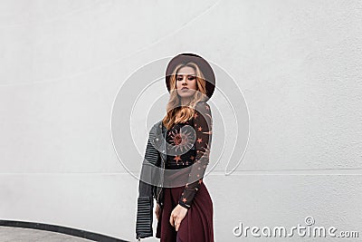 Attractive young woman in a vintage patterned blouse in an elegant purple cape hat in a black leather jacket standing Stock Photo