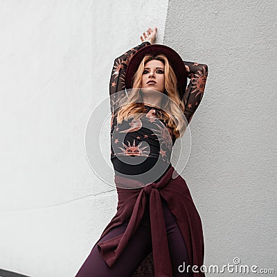 Attractive young woman in a vintage patterned blouse in an elegant purple hat in stylish pants in a purple cape posing Stock Photo