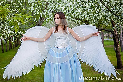 woman in a white corset and a blue puffy dress with large white angel wings behind her back Stock Photo