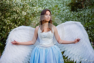 woman in a white corset and a blue puffy dress with large white angel wings behind her back Stock Photo