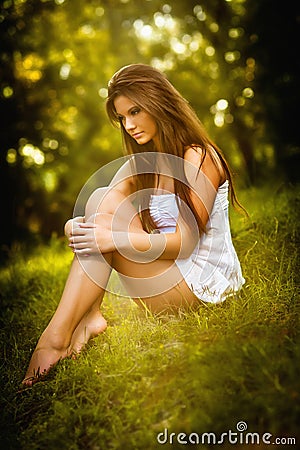 Attractive young woman in white short dress sitting on grass in a sunny summer day. Beautiful girl enjoying the nature Stock Photo