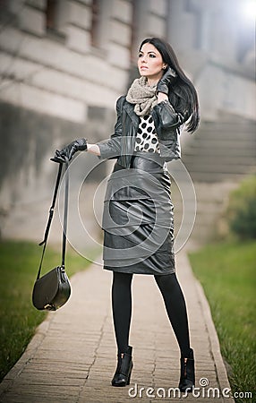 Attractive young woman in a winter fashion shot. Beautiful fashionable young girl in black leather outfit posing on avenue Stock Photo