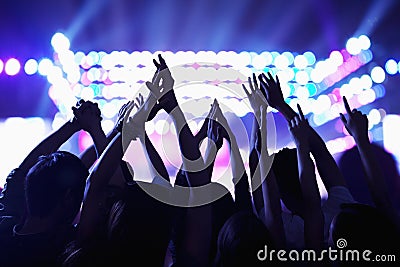 Audience watching a rock show, hands in the air, rear view, stage lights Stock Photo