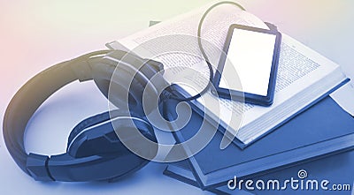 Audio book concept with headphones, tablet, open book and pile of books. Stock Photo