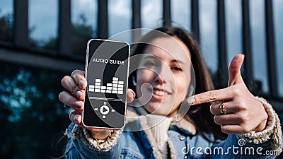 Audio tour online app on digital mobile smartphone. Happy young student woman holding phone listening audioguide Stock Photo