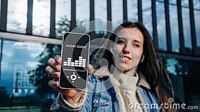 Audio tour online app on digital mobile smartphone. Happy young student woman holding phone listening audioguide Stock Photo