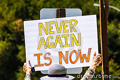 August 5, 2019 Palo Alto / CA / USA - Protester holding a sign with the message `Never again is now` at the rally against the curr Editorial Stock Photo