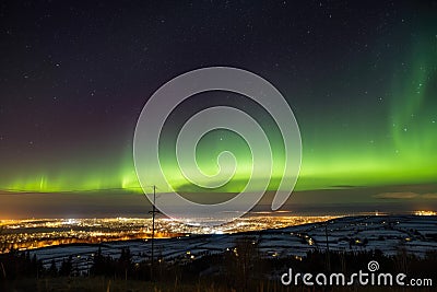 aurora dancing across starry night sky, with view of distant town visible in the foreground Stock Photo