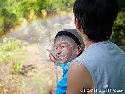 Authentic asian child boy smiling with happy face while making beautiful rainbow with father by water, sunlight Stock Photo