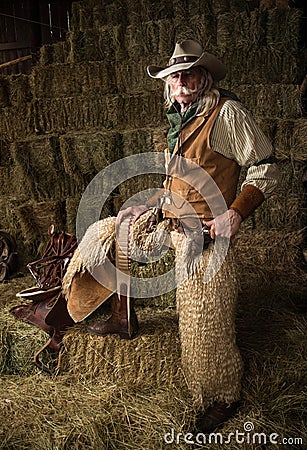 Authentic old west cowboy with shotgun, hat and bandanna in stable portrait Stock Photo