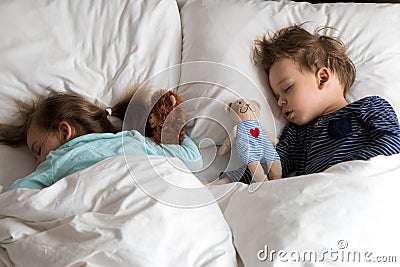 Authentic portrait cute caucasian little preschool siblings baby boy and girl in blue sleep with teddy bear on white bed Stock Photo
