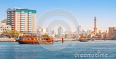 Authentic wooden cruise ship cruises and transports tourists along the Dubai Creek Canal with skyscrapers and minarets of Editorial Stock Photo