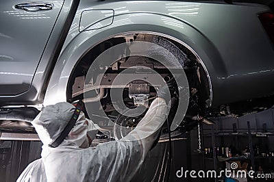 An auto mechanic applies anti-corrosion mastic to the underbody of a car. Stock Photo