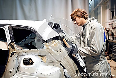 Auto repair worker flatten and align metal body car with hammer in garage Stock Photo