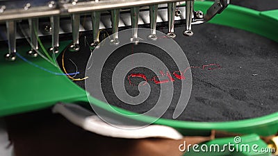 An automated machine embroiders pattern with red threads on a black cloth. Robotics works in tailoring production line Stock Photo