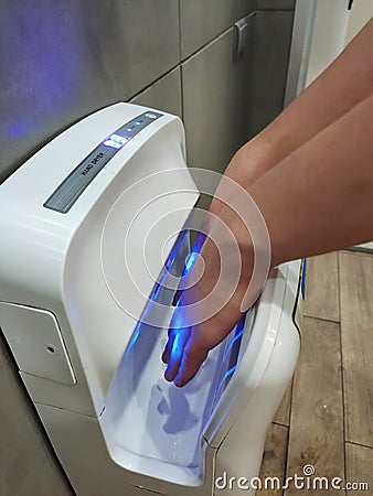 In a hand dryer in a public restroom, a man dries his hands after washing Stock Photo