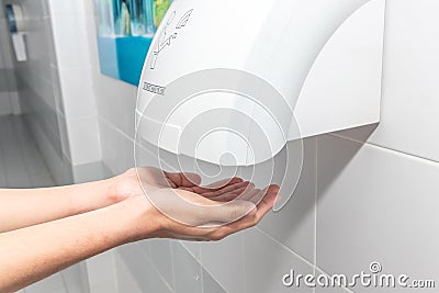 Automatic hand dryer in public toilet or restroom hygiene concept. A man hands using utomatic hand dryer in bathroom Stock Photo