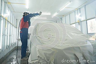 Automobile repairman painter in protective workwear and respirator painting car body in paint chamber. Automobile repair. Car Stock Photo