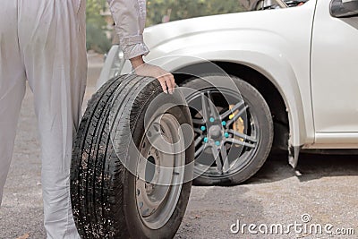 Automotive mechanic man carrying spare tire preparing change a wheel of car. Auto repair service. Stock Photo