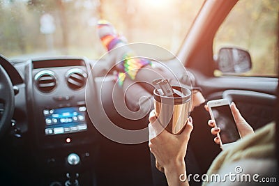 Autumn, Auto travel. Cose-up of a woman drinking take away cup coffee during the road trip in a car. Woman feet in warm Stock Photo