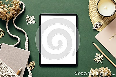 Autumn composition. Digital tablet mockup with blank screen, macrame handbag, candle, dried flowers on green background. Aesthetic Stock Photo