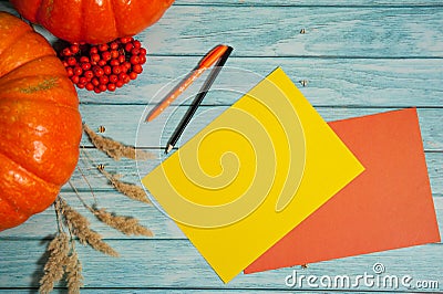 Two orange pumpkins, two sheets of blank paper, a pen and pencil, Rowan berries and dried cereals on a light blue wooden backgroun Stock Photo