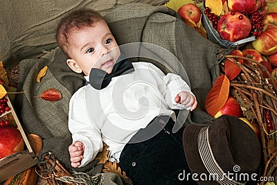 Autumn concept - child boy lie on yellow leaves with fruits and vegetables, red apples and pumpkins Stock Photo