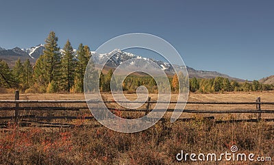 Autumn country landscape with a fence, snowy mountains and forest Stock Photo