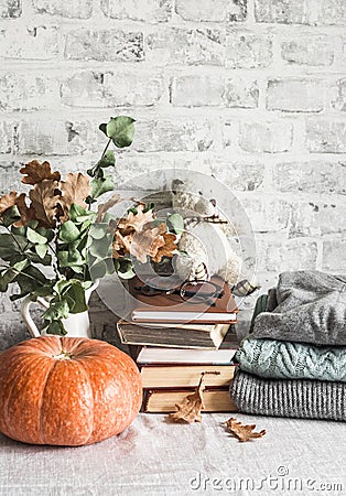 Autumn cozy home still life. Pumpkin, dry branch pitcher, stack of books, pile of winter autumn sweaters, teddy bear on the Stock Photo