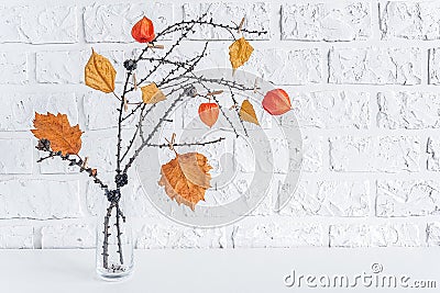 Autumn creative bouquet of branches with yellow leaves on clothespins in vase on table background white brick wall Copy space Stock Photo