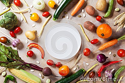 Autumn farm vegetables, root crops and white plate top view with copy space for menu or recipe. Healthy food on kitchen table. Stock Photo