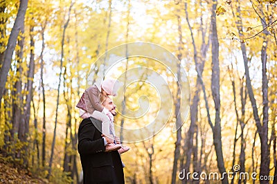 Autumn fashion for children and the whole family. A small daughter sits on the shoulders of the father in the neck against the bac Stock Photo