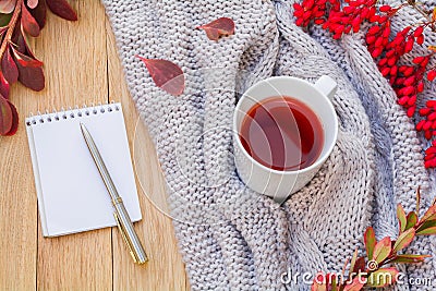 Autumn flatlay on a wooden background with a cup of tea and branches of barberry. Notepad with pen on the table. Home coziness Stock Photo