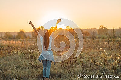 Autumn Girl enjoying nature on the field. Beauty Girl Outdoors raising hands in sunlight rays. Beautiful Teenage Model girl Stock Photo