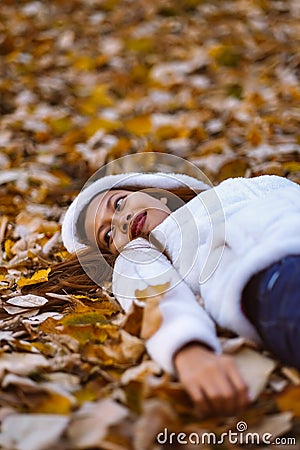 Autumn girl playing in city park. Portrait of an autumn woman lying over leaves and smiling outside in fall forest. Beautiful ener Stock Photo