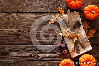 Autumn harvest or thanksgiving table scene with silverware, napkin, leaves and pumpkin border against a rustic wood background Stock Photo