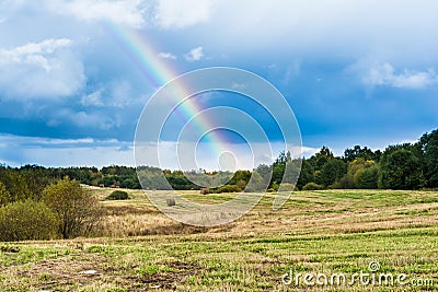 Autumn landscape with cloudy weather, large rainy clouds over a chamfered yellow field, the rainbow is in the sky Stock Photo