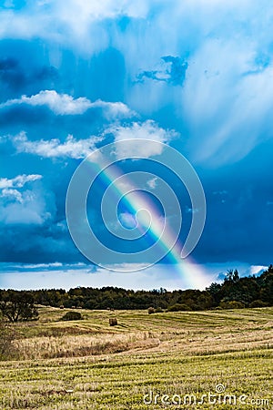 Autumn landscape with cloudy weather, large rainy clouds over a chamfered yellow field, the rainbow is in the sky Stock Photo