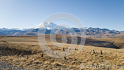 Autumn landscape. View of the dry yellow field and the beautiful mount Elbrus in the Caucasus. Pyramids of stones Stock Photo