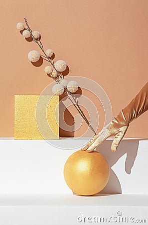 Autumn minimalistic scene, Hand in golden gloves, decor cube, ball and dry brunch in styish beige geometry space. Seasonal fall Stock Photo