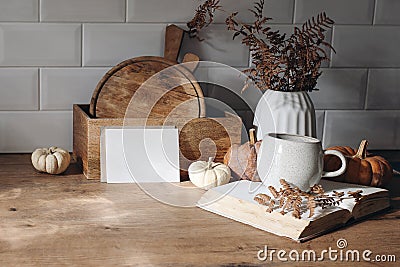 Autumn mockup scene. Blank card, open book, cup of coffee, wooden chop boards and dry fern leaves in sunlight. Fall Stock Photo