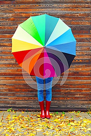 Autumn photo woman holding colorful umbrella wearing a red rubber boots over wooden background Stock Photo