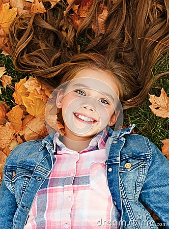Autumn portrait of adorable smiling little girl child preteen lying in leaves in the park Stock Photo