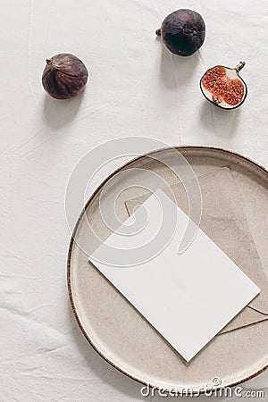 Autumn still life. Blank greeting card mockup, cut figs fruit and ceramic plate on white linen table cloth background Stock Photo