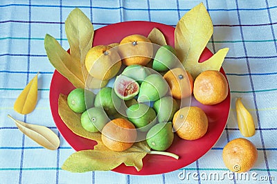 Ripe fig fruits and tangerines on the plate with yellow leaves Stock Photo