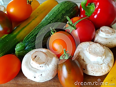 A close-up. Vegetable still life on a cutting board. Zucchini, tomatoes, champignons, peppers. Red, yellow, orange. Stock Photo